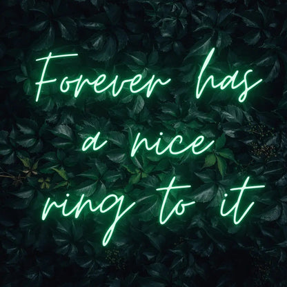 Forever Has a Nice Ring to It LED Neon Light Sign in green, featuring three lines of script lettering against a dark foliage backdrop.