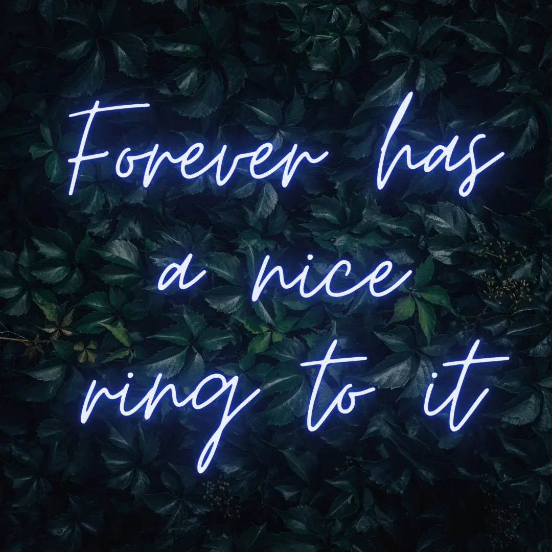 Forever Has a Nice Ring to It LED Neon Light Sign in blue, featuring three lines of script lettering against a dark foliage backdrop.