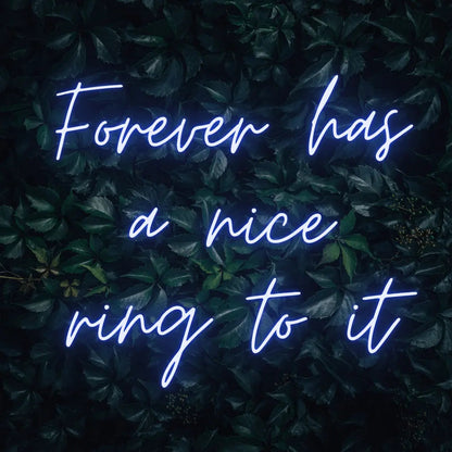Forever Has a Nice Ring to It LED Neon Light Sign in blue, featuring three lines of script lettering against a dark foliage backdrop.