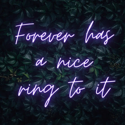 Forever Has a Nice Ring to It LED Neon Light Sign in purple, featuring three lines of script lettering against a dark foliage backdrop.