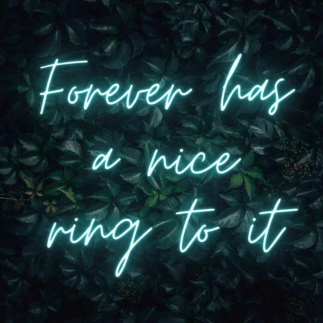 Forever Has a Nice Ring to It LED Neon Light Sign in turquoise, featuring three lines of script lettering against a dark foliage backdrop.