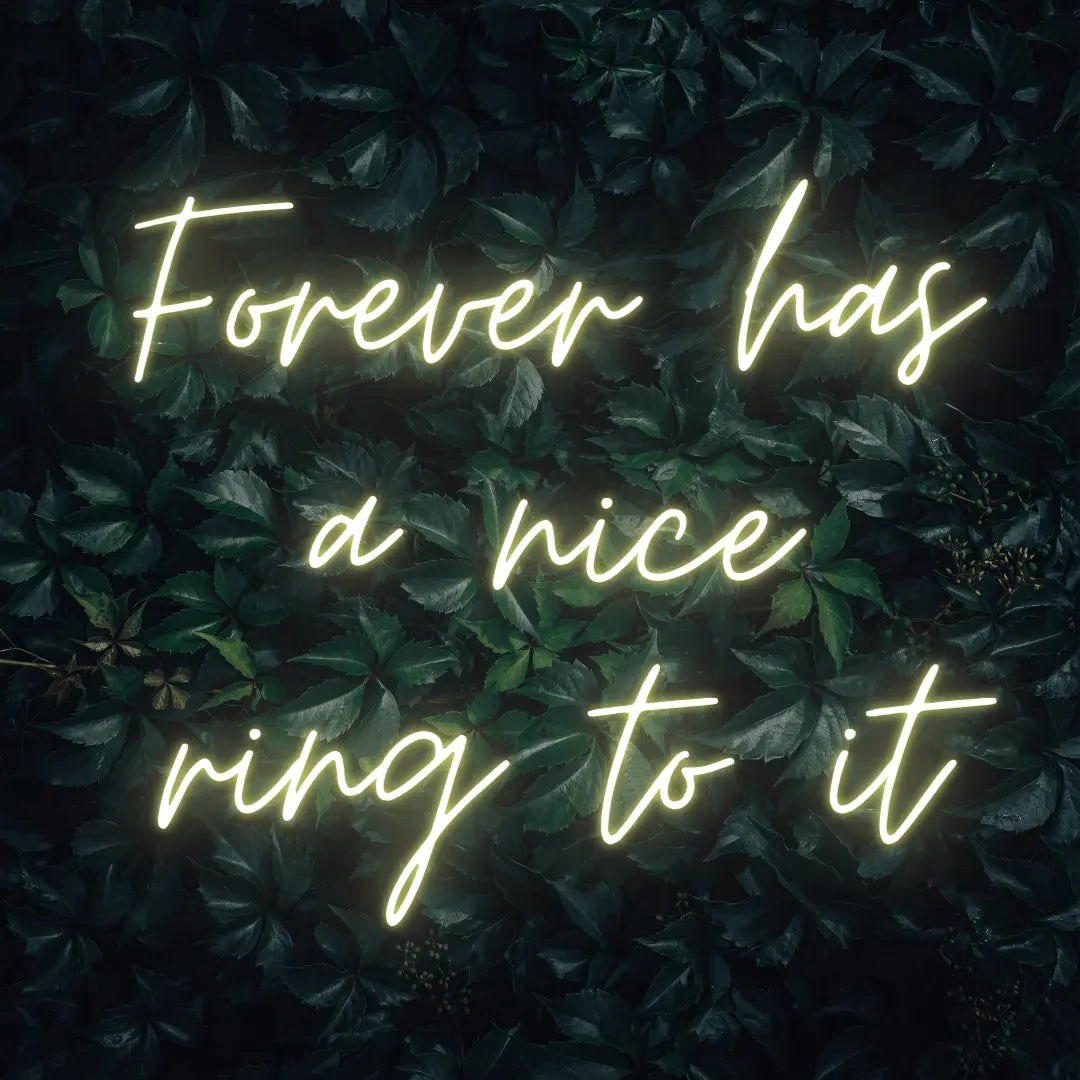 Forever Has a Nice Ring to It LED Neon Light Sign in warm white, featuring three lines of script lettering against a dark foliage backdrop.