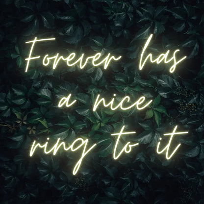 Forever Has a Nice Ring to It LED Neon Light Sign in warm white, featuring three lines of script lettering against a dark foliage backdrop.