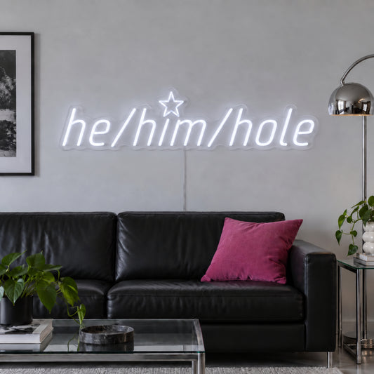He/Him/Hole Neon Sign in white, featuring He/Him/Hole script lettering above a dark sofa.