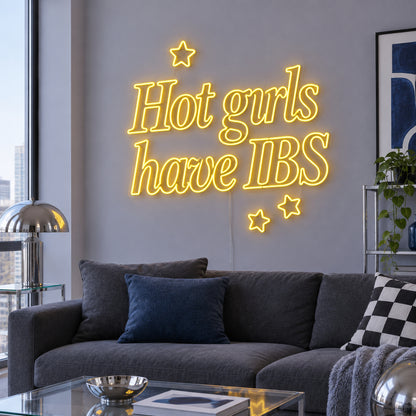 Hot Girls Have IBS Neon Sign in yellow with star details above a charcoal sofa.