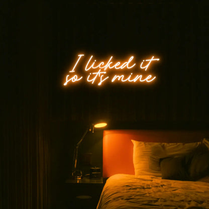 I Licked It So Its Mine LED Neon Light Sign in orange, featuring two lines of script lettering illuminated above a bed.