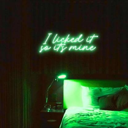 I Licked It So Its Mine LED Neon Light Sign in green, featuring two lines of script lettering illuminated above a bed.