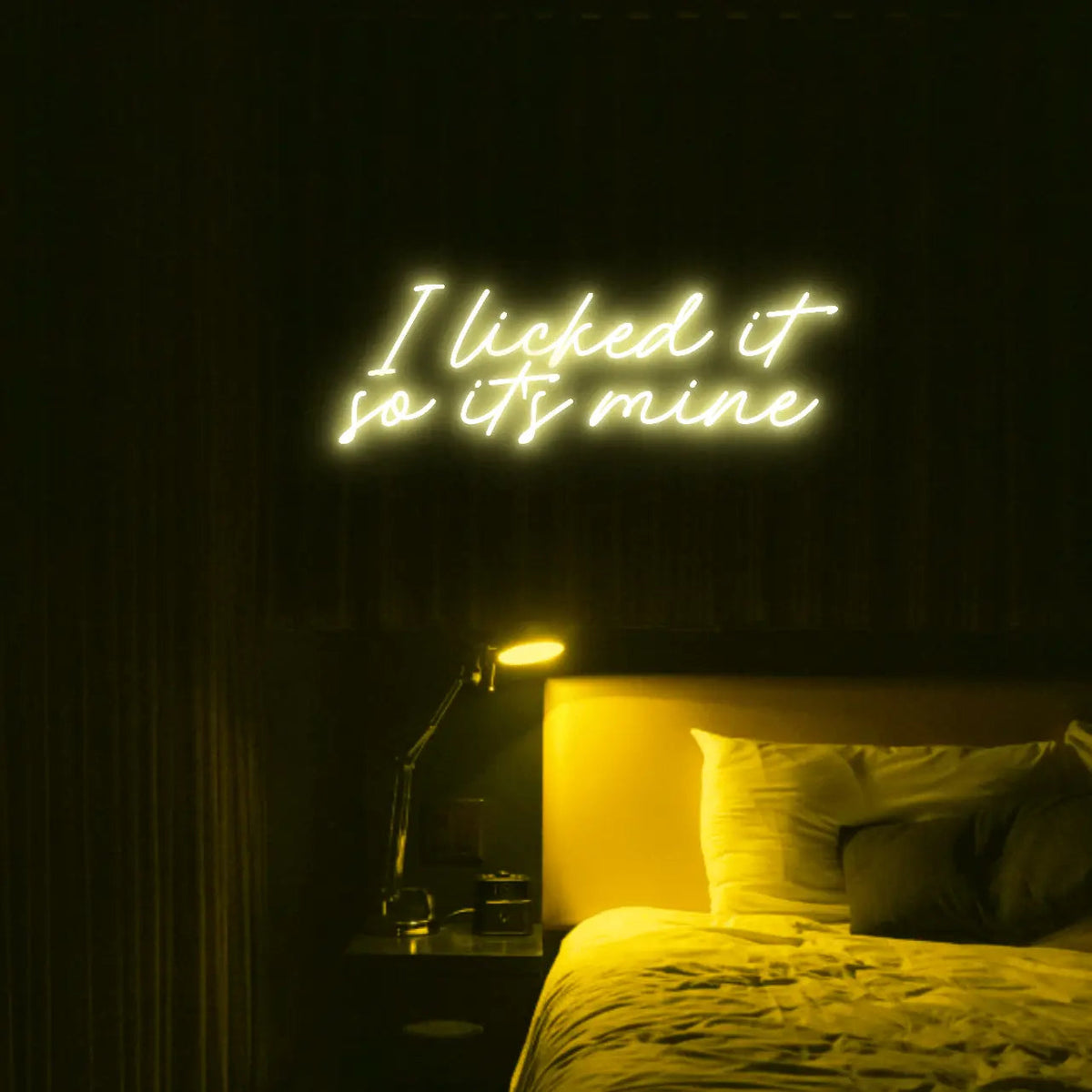 I Licked It So Its Mine LED Neon Light Sign in yellow, featuring two lines of script lettering illuminated above a bed.