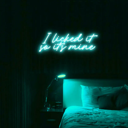 I Licked It So Its Mine LED Neon Light Sign in turquoise, featuring two lines of script lettering illuminated above a bed.