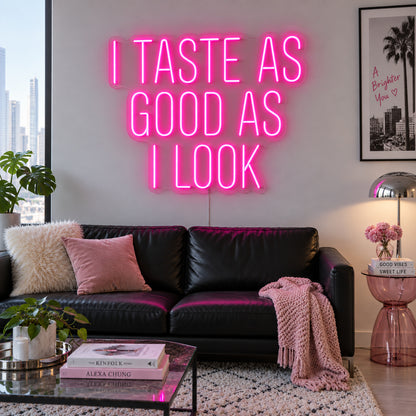 Rose Red version of the I Taste As Good As I Look Neon Sign, shown above a black sofa.