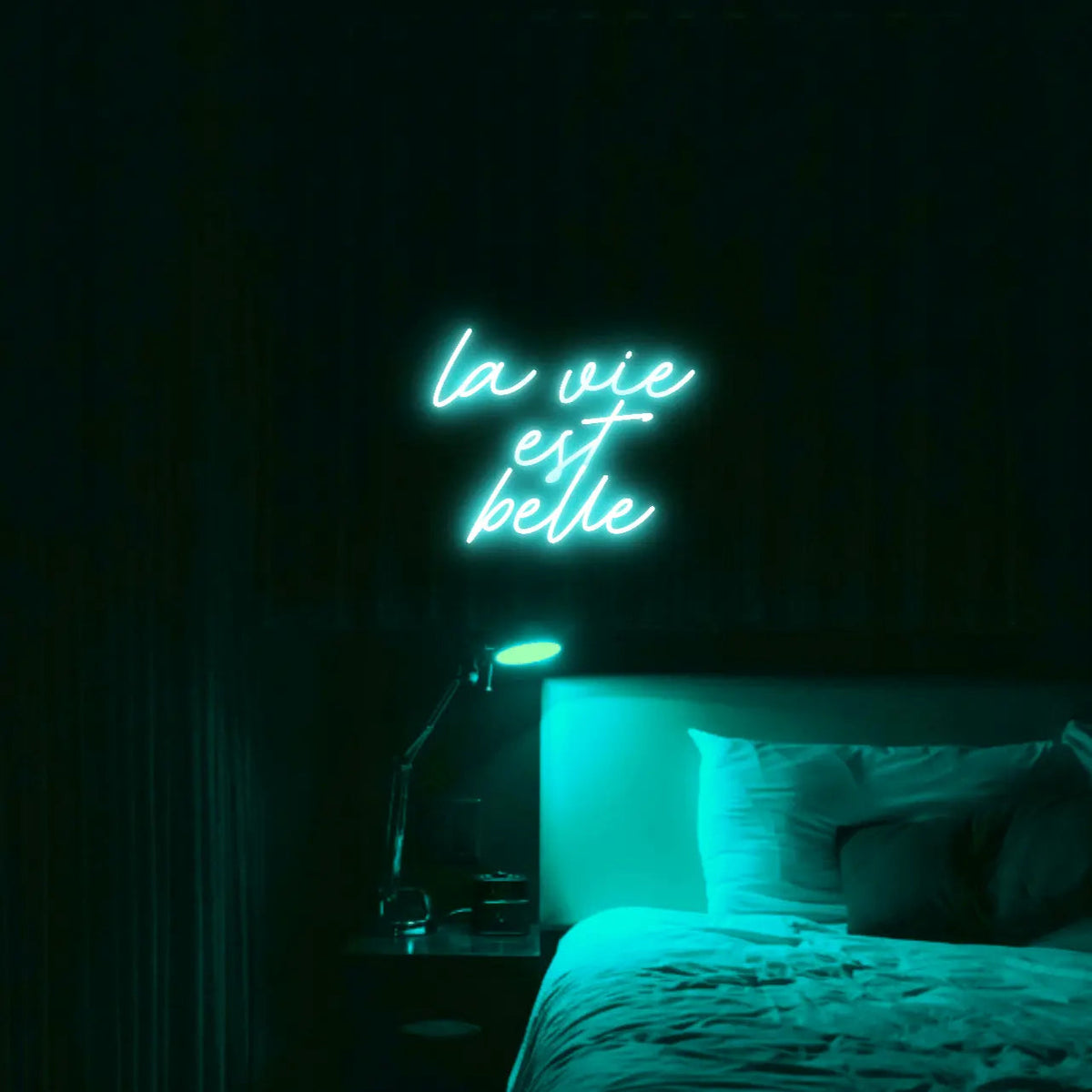 La Vie est Belle LED Neon Light Sign in turquoise, featuring script lettering illuminated above a bed.
