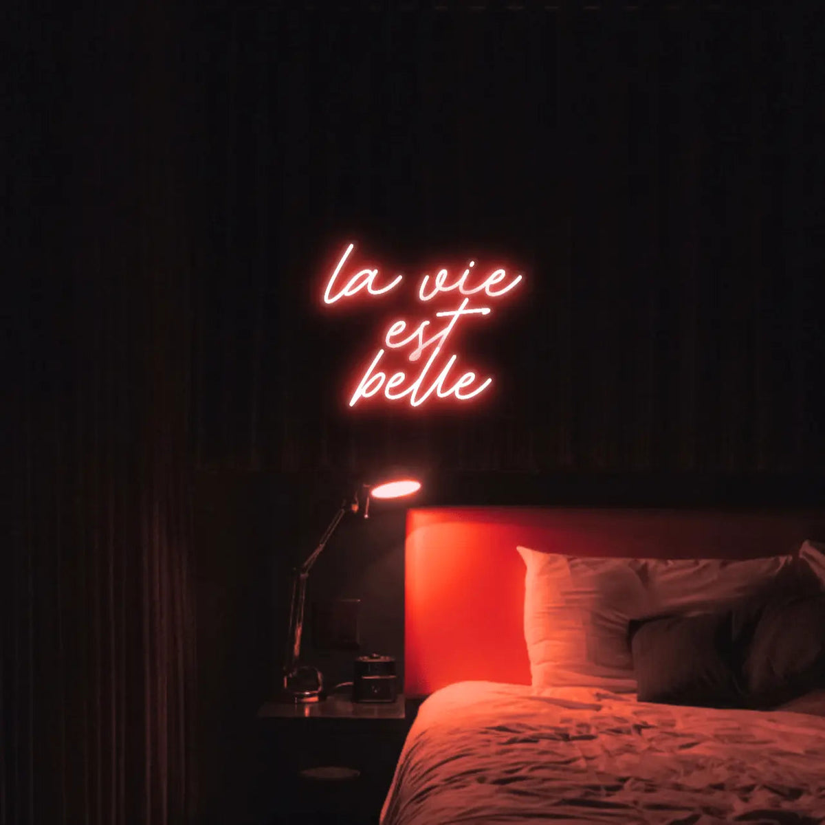 La Vie est Belle LED Neon Light Sign in red, featuring script lettering illuminated above a bed.