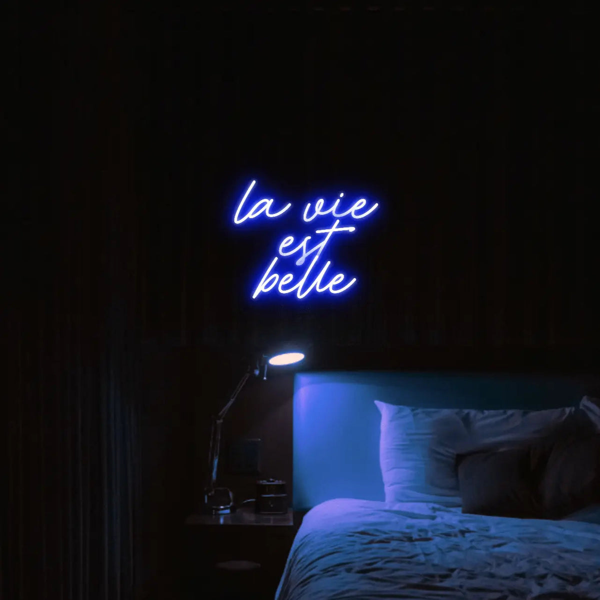La Vie est Belle LED Neon Light Sign in blue, featuring script lettering illuminated above a bed.