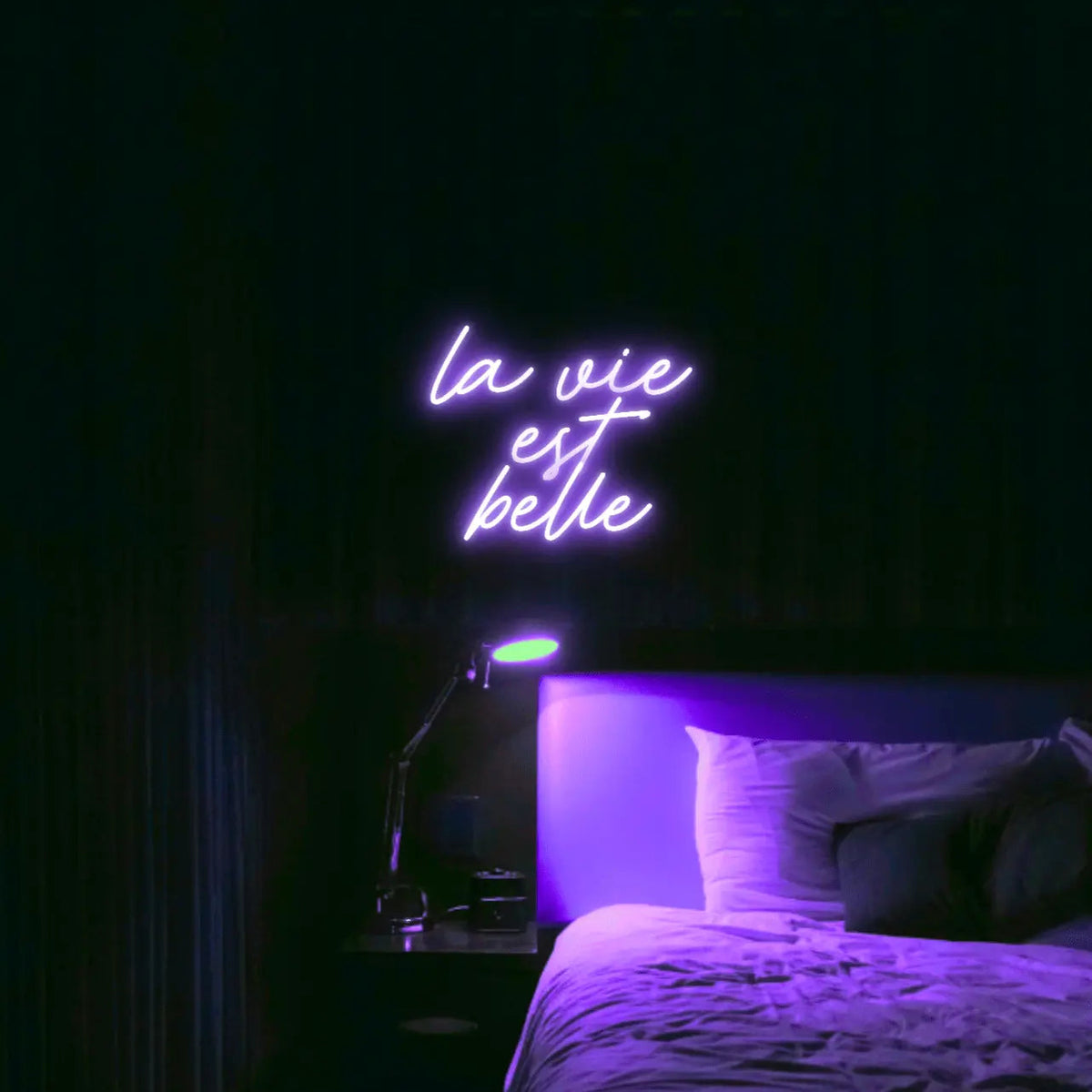 La Vie est Belle LED Neon Light Sign in purple, featuring script lettering illuminated above a bed.