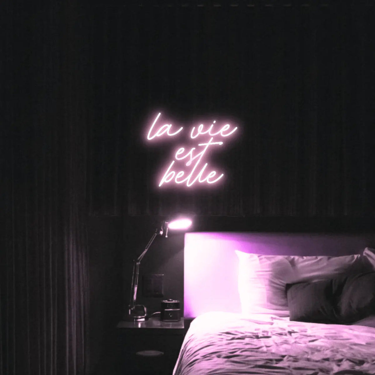 La Vie est Belle LED Neon Light Sign in pale pink, featuring script lettering illuminated above a bed.