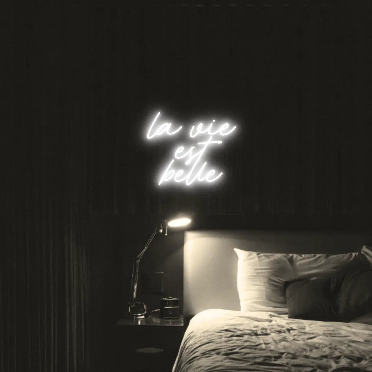 La Vie est Belle LED Neon Light Sign in white, featuring script lettering illuminated above a bed.