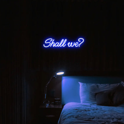 Shall we? LED Neon Light Sign in blue, featuring script lettering illuminated above a bed.