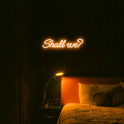 Shall we? LED Neon Light Sign in orange, featuring script lettering illuminated above a bed.