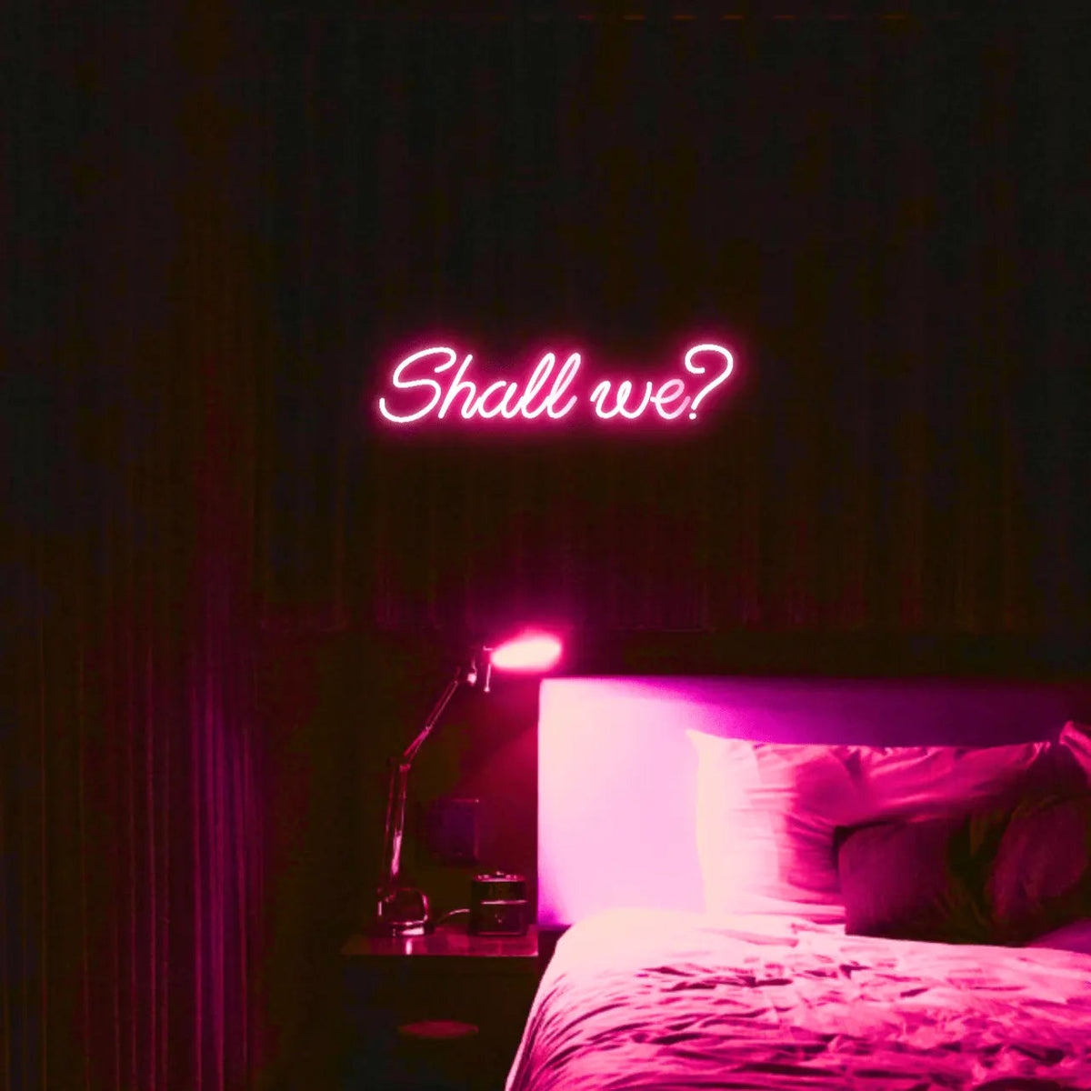 Shall we? LED Neon Light Sign in pink, featuring script lettering illuminated above a bed.