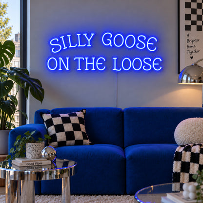 Silly Goose On The Loose Neon Sign glowing blue above a blue sofa with checkered cushions.