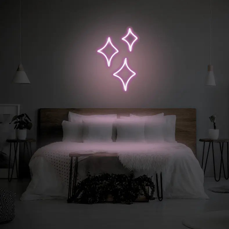 Sparkle LED Neon Light Sign in pale pink, featuring three outlined sparkle shapes illuminated above a bed.