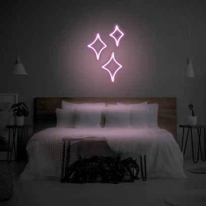 Sparkle LED Neon Light Sign in pale pink, featuring three outlined sparkle shapes illuminated above a bed.