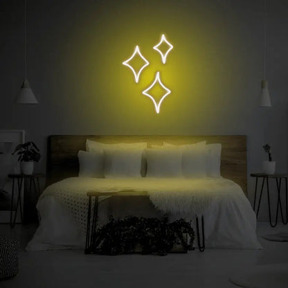 Sparkle LED Neon Light Sign in yellow, featuring three outlined sparkle shapes illuminated above a bed.