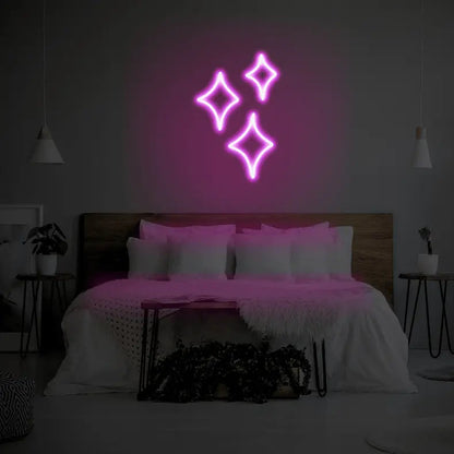 Sparkle LED Neon Light Sign in pink, featuring three outlined sparkle shapes illuminated above a bed.