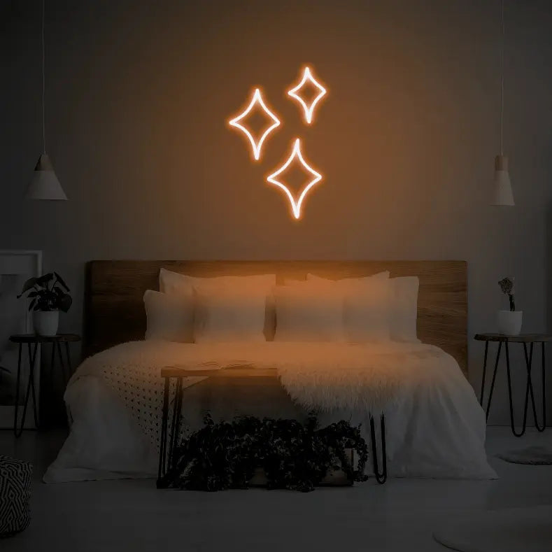 Sparkle LED Neon Light Sign in orange, featuring three outlined sparkle shapes illuminated above a bed.
