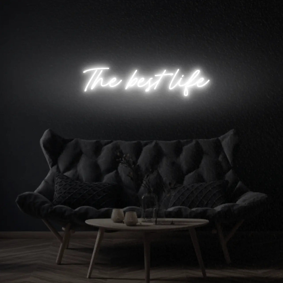 The Best Life LED Neon Light Sign in white, featuring script lettering illuminated above a dark tufted sofa.