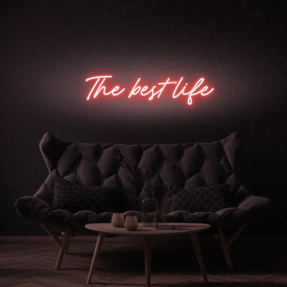 The Best Life LED Neon Light Sign in red, featuring script lettering illuminated above a dark tufted sofa.