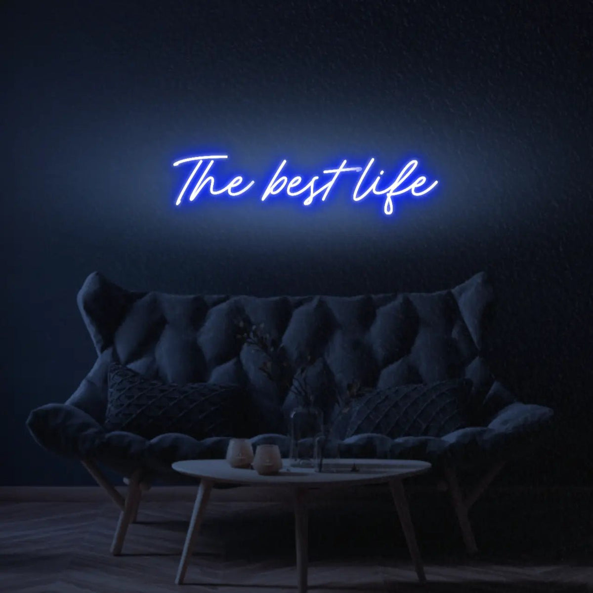 The Best Life LED Neon Light Sign in blue, featuring script lettering illuminated above a dark tufted sofa.