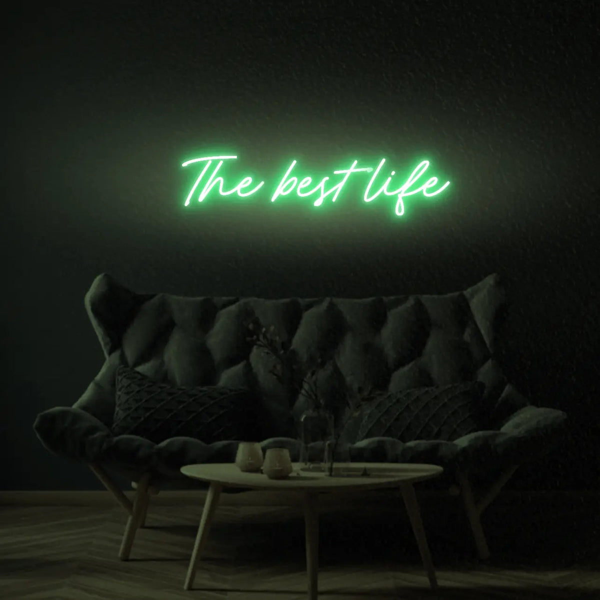 The Best Life LED Neon Light Sign in green, featuring script lettering illuminated above a dark tufted sofa.