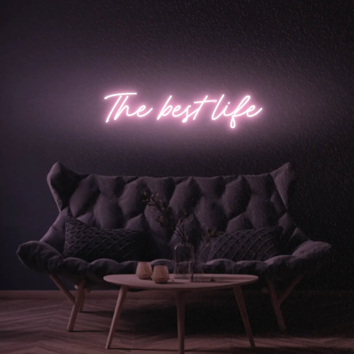 The Best Life LED Neon Light Sign in pale pink, featuring script lettering illuminated above a dark tufted sofa.
