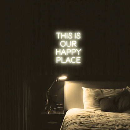 This is our happy place LED Neon Light Sign in warm white, featuring stacked block lettering illuminated above a bed.