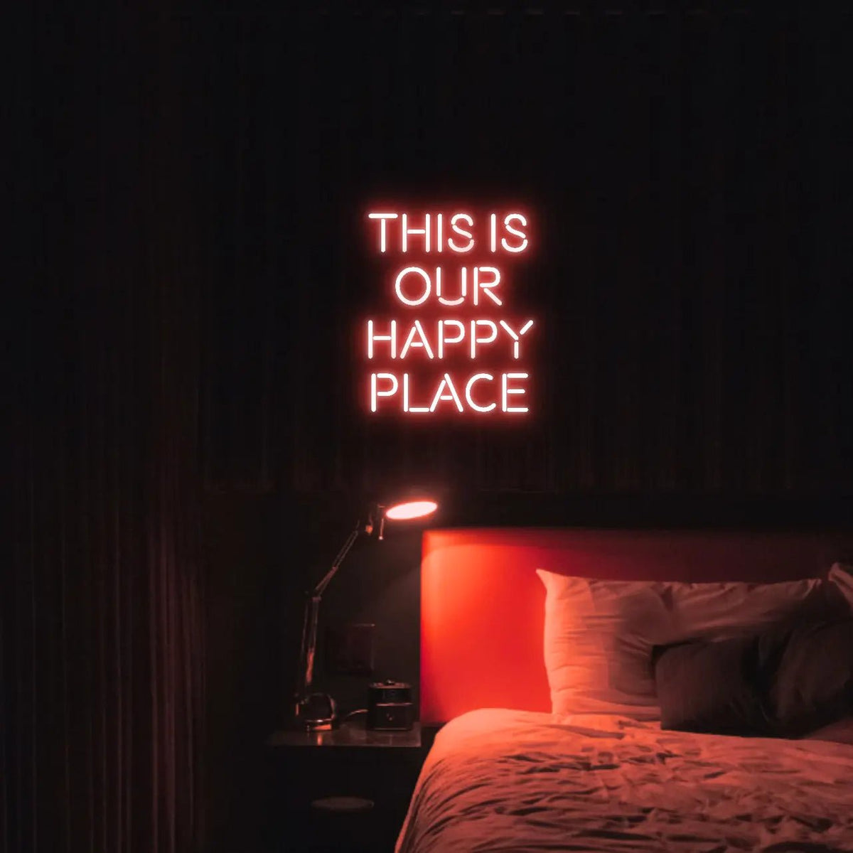 This is our happy place LED Neon Light Sign in red, featuring stacked block lettering illuminated above a bed.