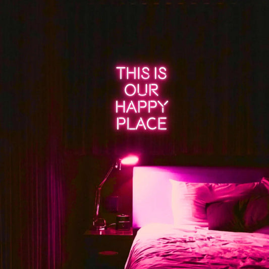 This is our happy place LED Neon Light Sign in pink, featuring stacked block lettering illuminated above a bed.