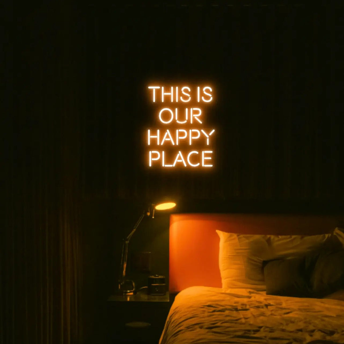 This is our happy place LED Neon Light Sign in orange, featuring stacked block lettering illuminated above a bed.