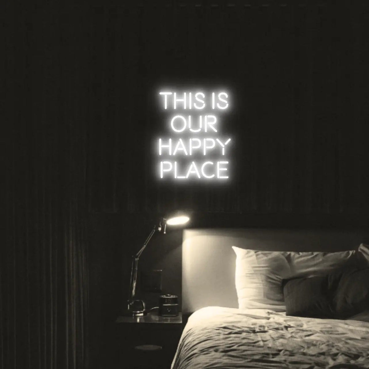 This is our happy place LED Neon Light Sign in white, featuring stacked block lettering illuminated above a bed.