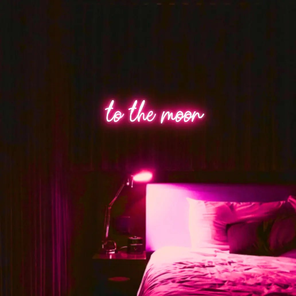 To The Moon LED Neon Light Sign in pink, featuring script lettering illuminated above a bed in a dark bedroom.