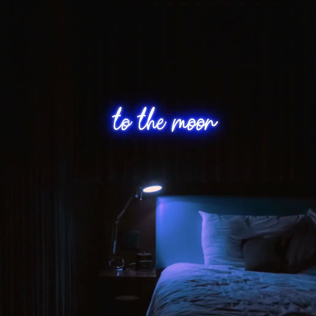 To The Moon LED Neon Light Sign in blue, featuring script lettering illuminated above a bed in a dark bedroom.