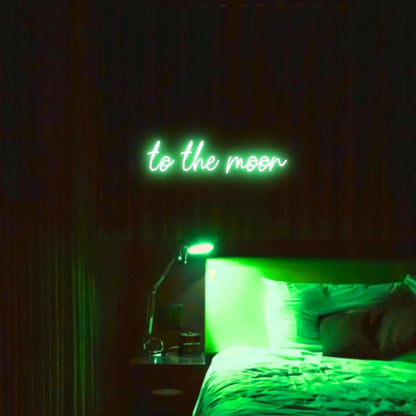 To The Moon LED Neon Light Sign in green, featuring script lettering illuminated above a bed in a dark bedroom.