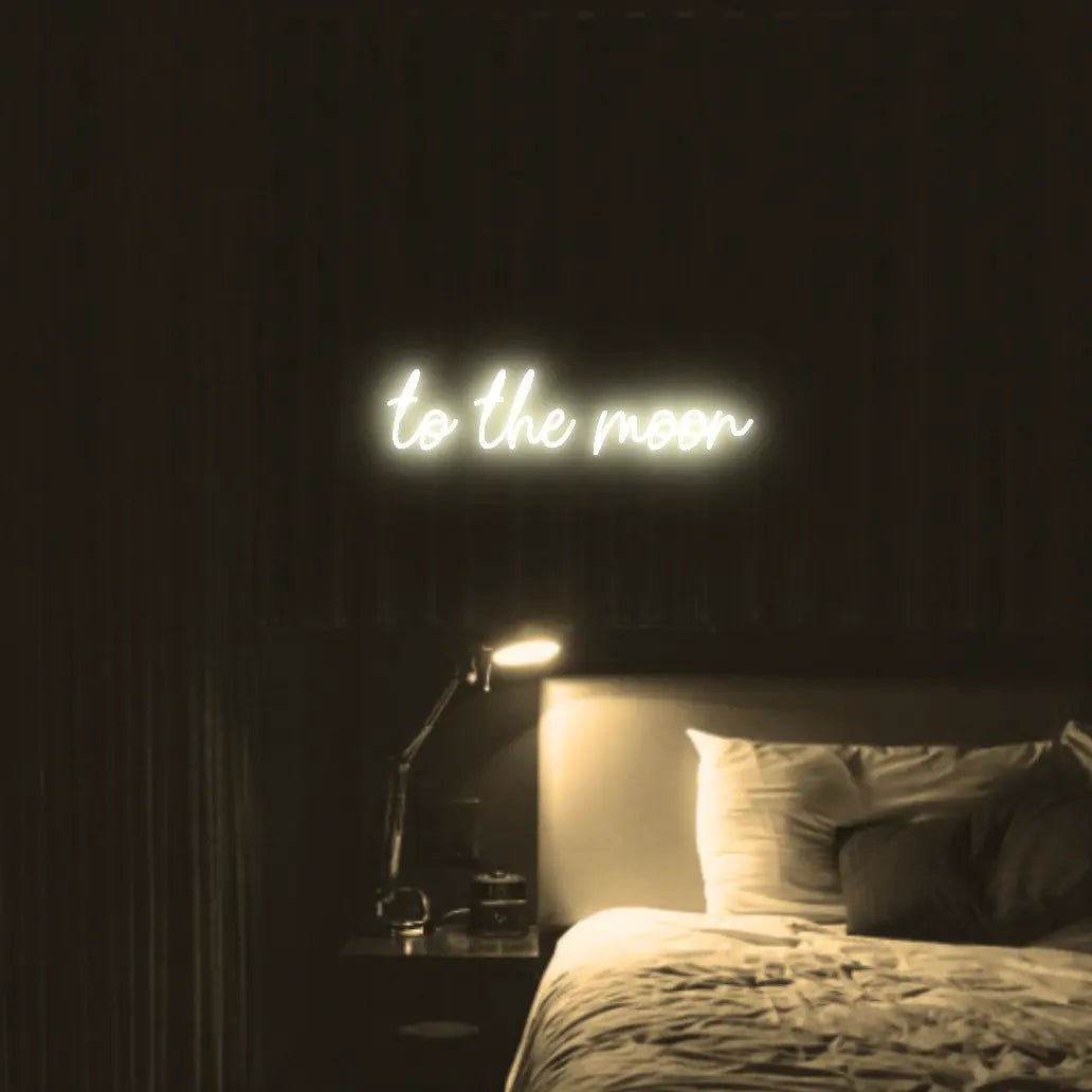 To The Moon LED Neon Light Sign in warm white, featuring script lettering illuminated above a bed in a dark bedroom.