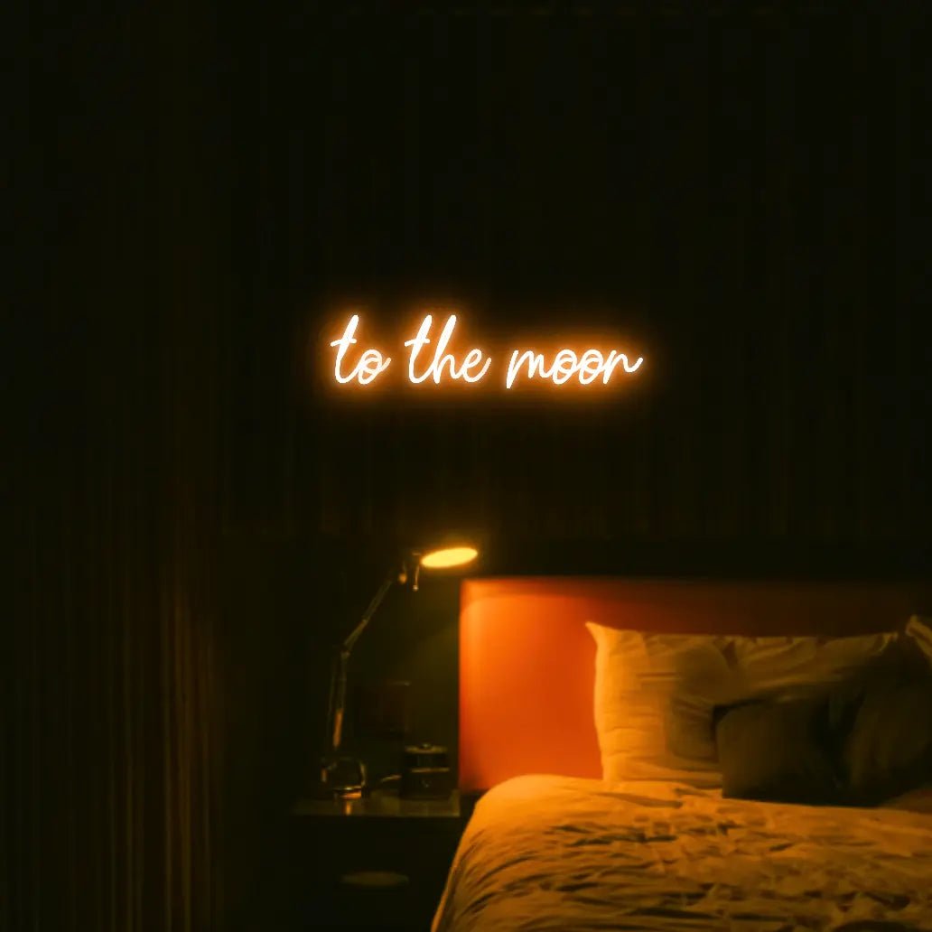 To The Moon LED Neon Light Sign in orange, featuring script lettering illuminated above a bed in a dark bedroom.