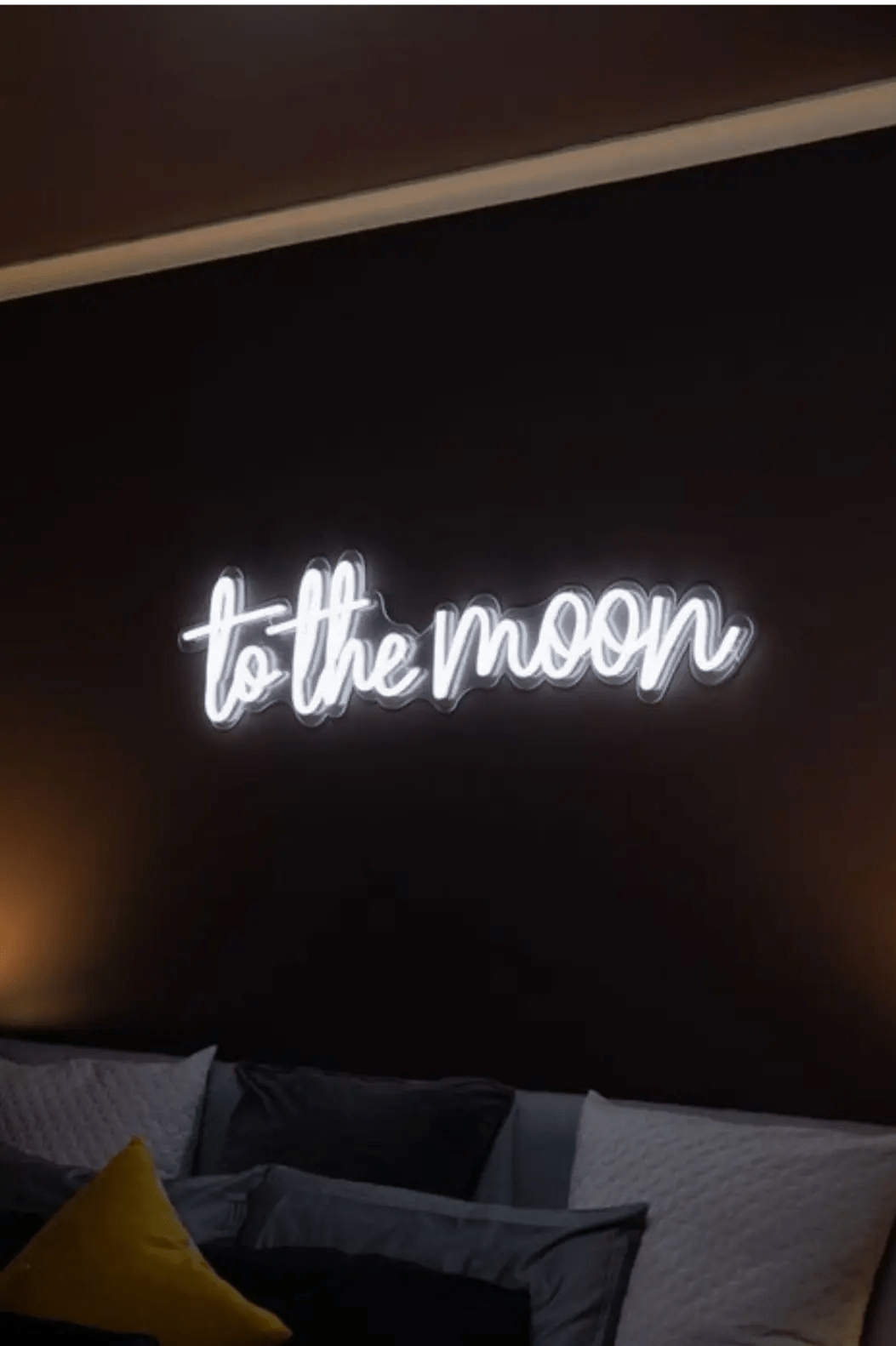 To The Moon LED Neon Light Sign in white, featuring script lettering on a bedroom wall above a sofa.
