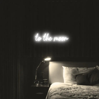 To The Moon LED Neon Light Sign in white, featuring script lettering illuminated above a bed in a dark bedroom.