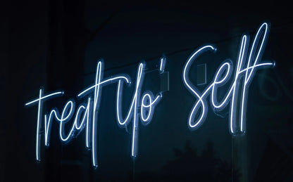 Treat Yo'self LED Neon Light Sign in light blue, featuring script lettering viewed at an angle against a dark wall.