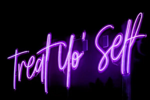 Treat Yo'self LED Neon Light Sign in purple, featuring script lettering viewed at an angle against a dark wall.