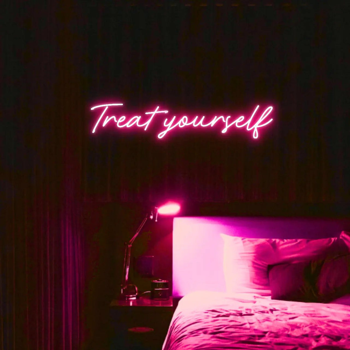 Treat Yourself LED Neon Light Sign in pink, featuring script lettering illuminated above a bed in a dark bedroom.