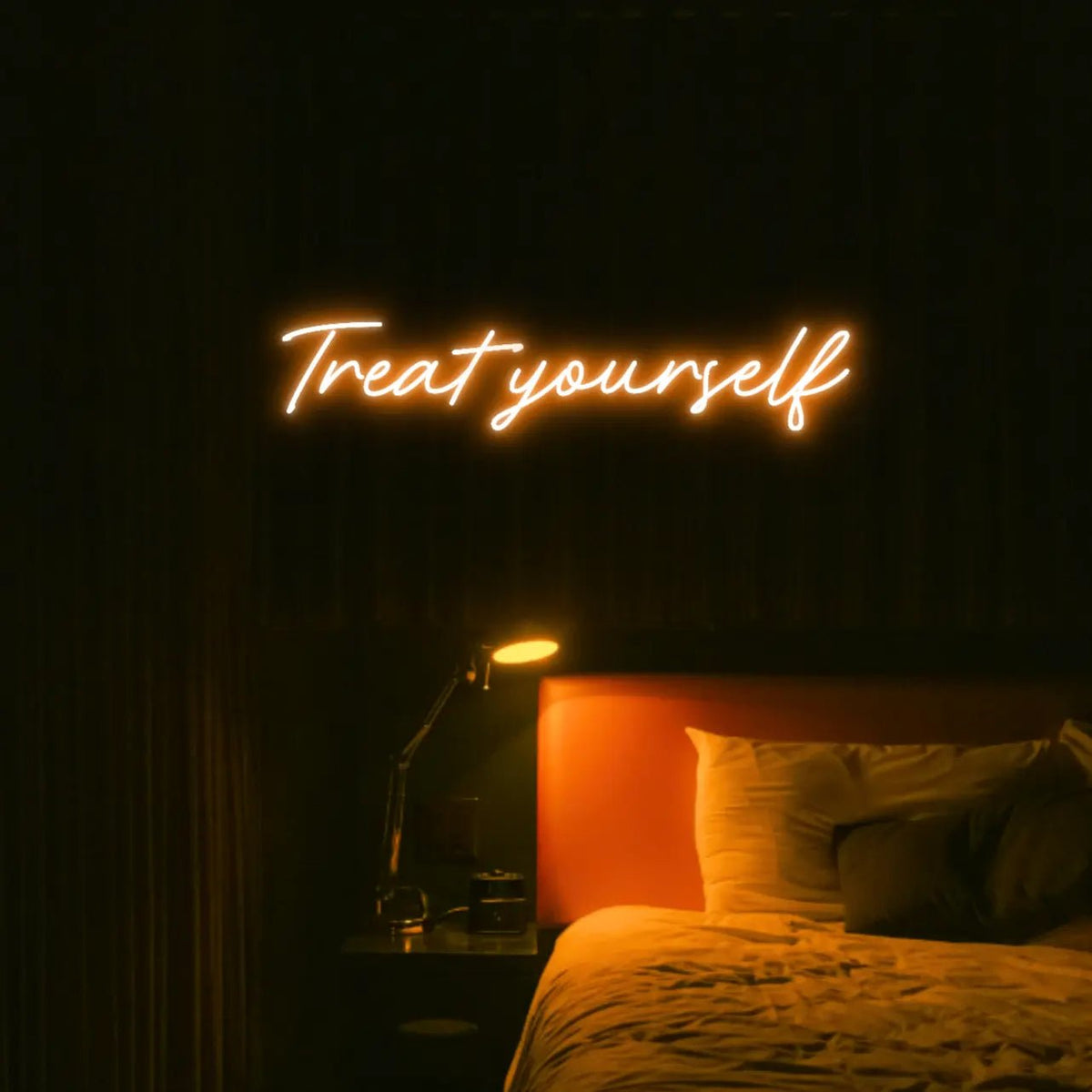 Treat Yourself LED Neon Light Sign in orange, featuring script lettering illuminated above a bed in a dark bedroom.